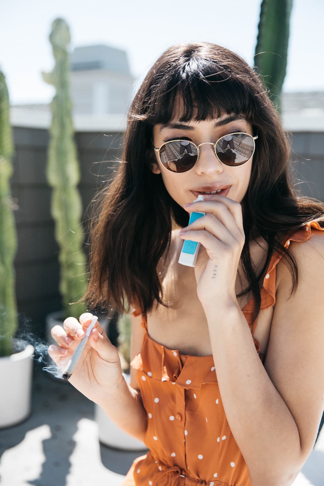 Woman in an orange polka-dot dress and sunglasses using a PHILTER device on a sunny rooftop